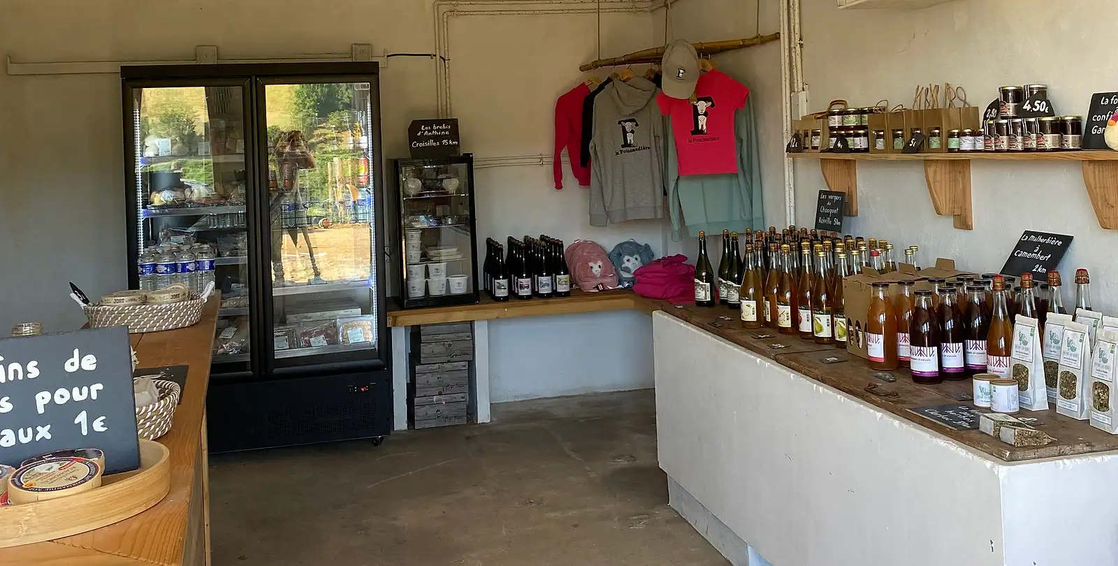 L'intérieur de la boutique de la Foucaudière : le comptoir, ses étagères de produits fermiers et les bouteilles des producteurs voisins