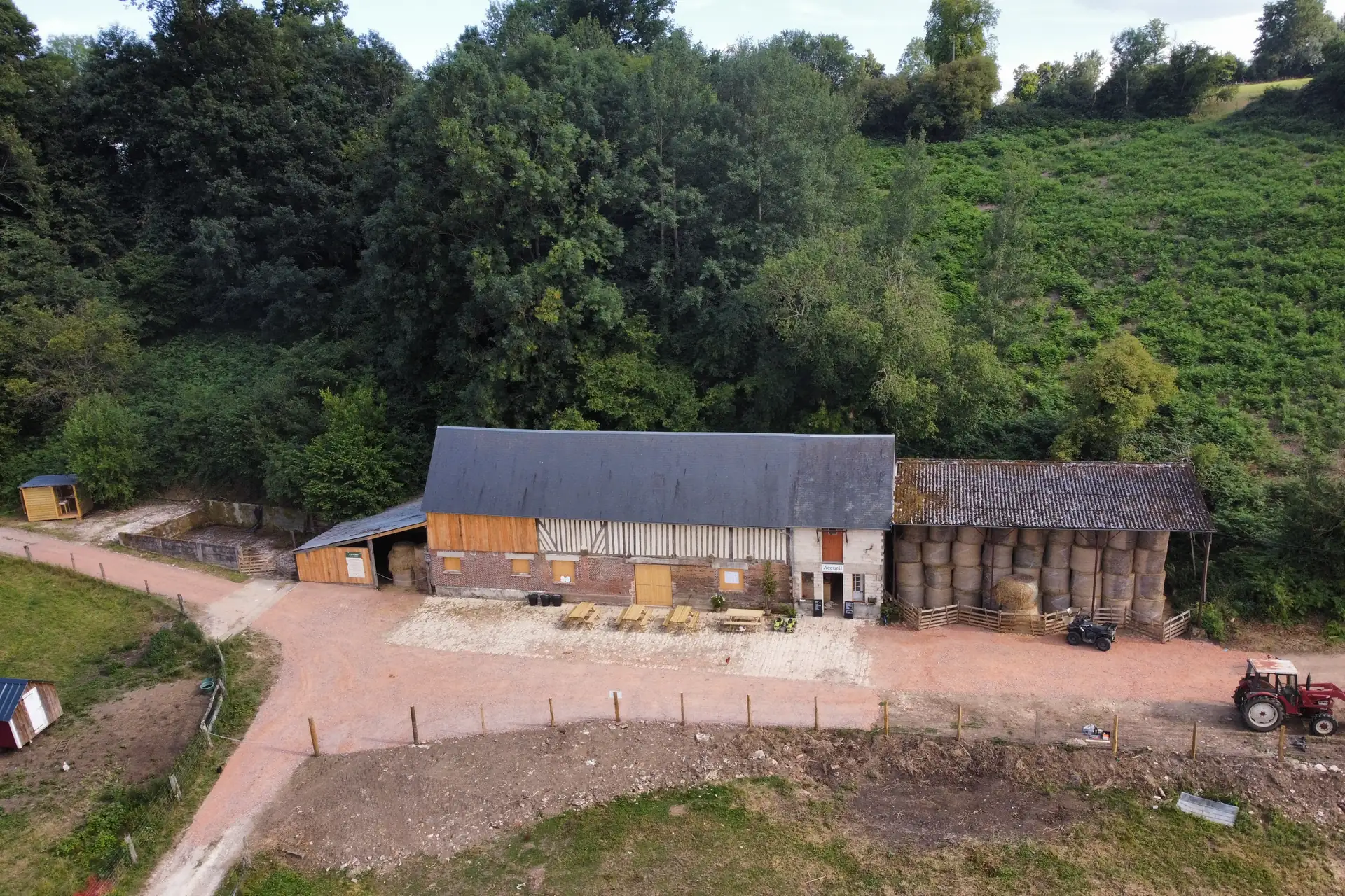 La cour de la ferme de la Foucaudière vue du ciel : la grande grange normande, l'accueil, les tables de pique-nique et le tracteur