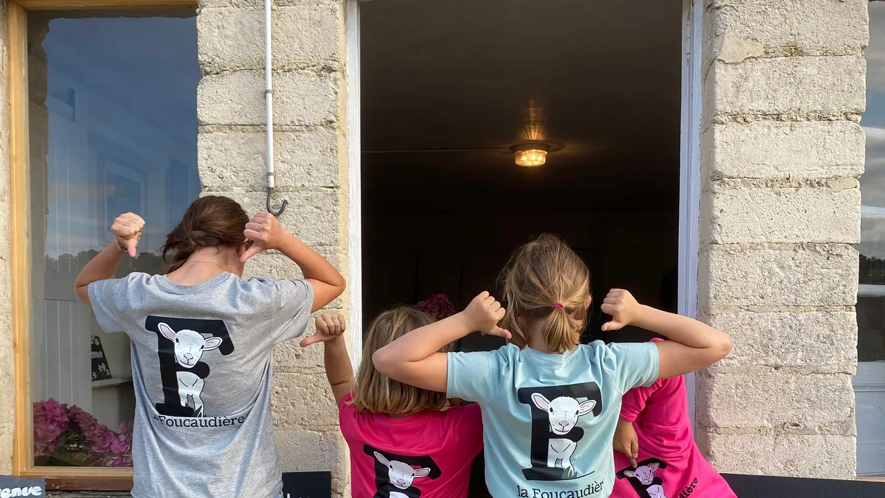 Quatre enfants en tee-shirt de la Foucaudière devant la porte de l'accueil de la ferme