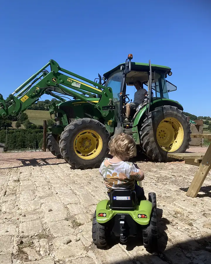 Un tout-petit sur son tracteur à pédales, devant le tracteur de la ferme de la Foucaudière