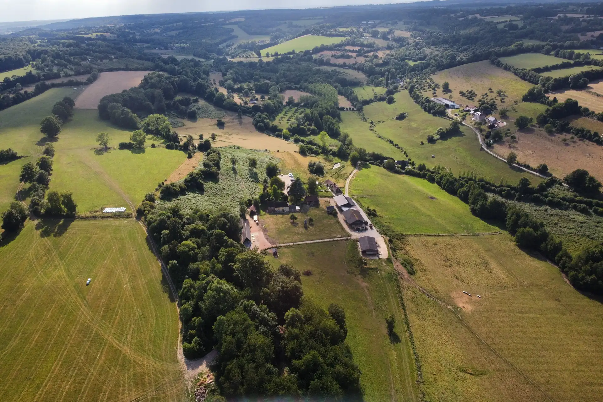 La ferme de la Foucaudière vue du ciel, ses bâtiments au milieu des prairies, des haies et des bois du Pays d'Auge