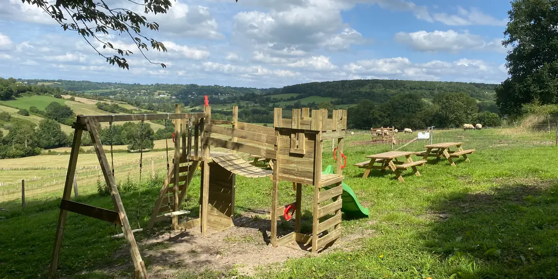 L'aire de jeux en bois et ses tables de pique-nique, face aux collines du Pays d'Auge