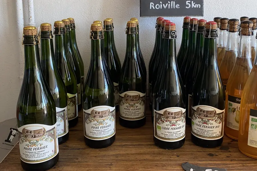 Bouteilles de cidre et de poiré fermiers d'un verger voisin, alignées sur le comptoir de la boutique