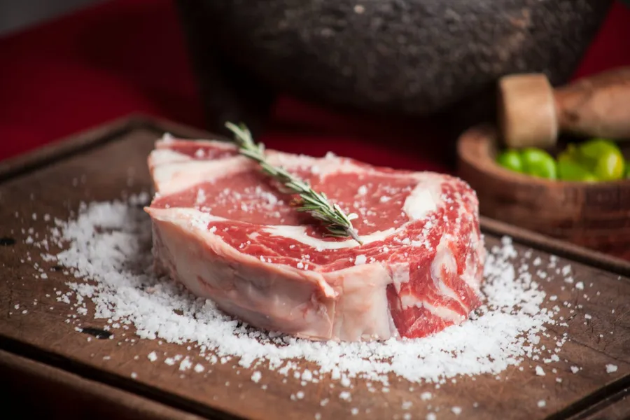 Une pièce de porc fermier sur une planche en bois, avec du gros sel et une branche de romarin