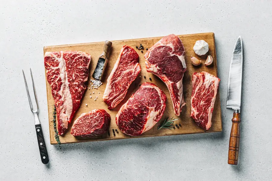 Pièces de viande fermière posées sur une planche de découpe, avec sel, ail et thym